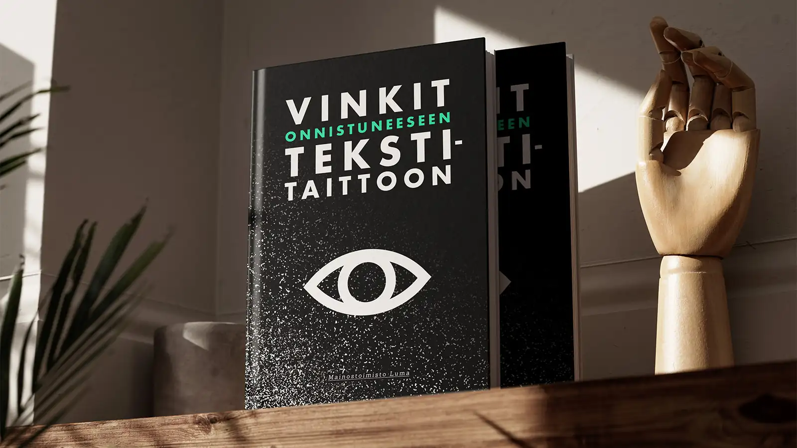 Luma Creativen blogiartikkelin kansikuva, jossa on mustakantinen kirja otsikolla ”VINKIT ONNISTUNEESEEN TEKSTITAITTOON”. Kirjan kannessa on suuri silmäsymboli ja taustalla näkyy tyylitelty puinen käsi ja kasveja pehmeässä luonnonvalossa.