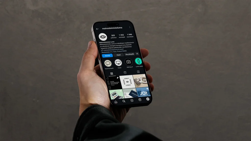 Luma Creativen blogiartikkelin pääkuva, jossa kädessä pidetään älypuhelinta (mobiilinäkymä) harmaata betoniseinää vasten. Kuvitus visualisoi PK-yritysten sosiaalisen median läsnäoloa ja brändinhallintaa vuonna 2025.