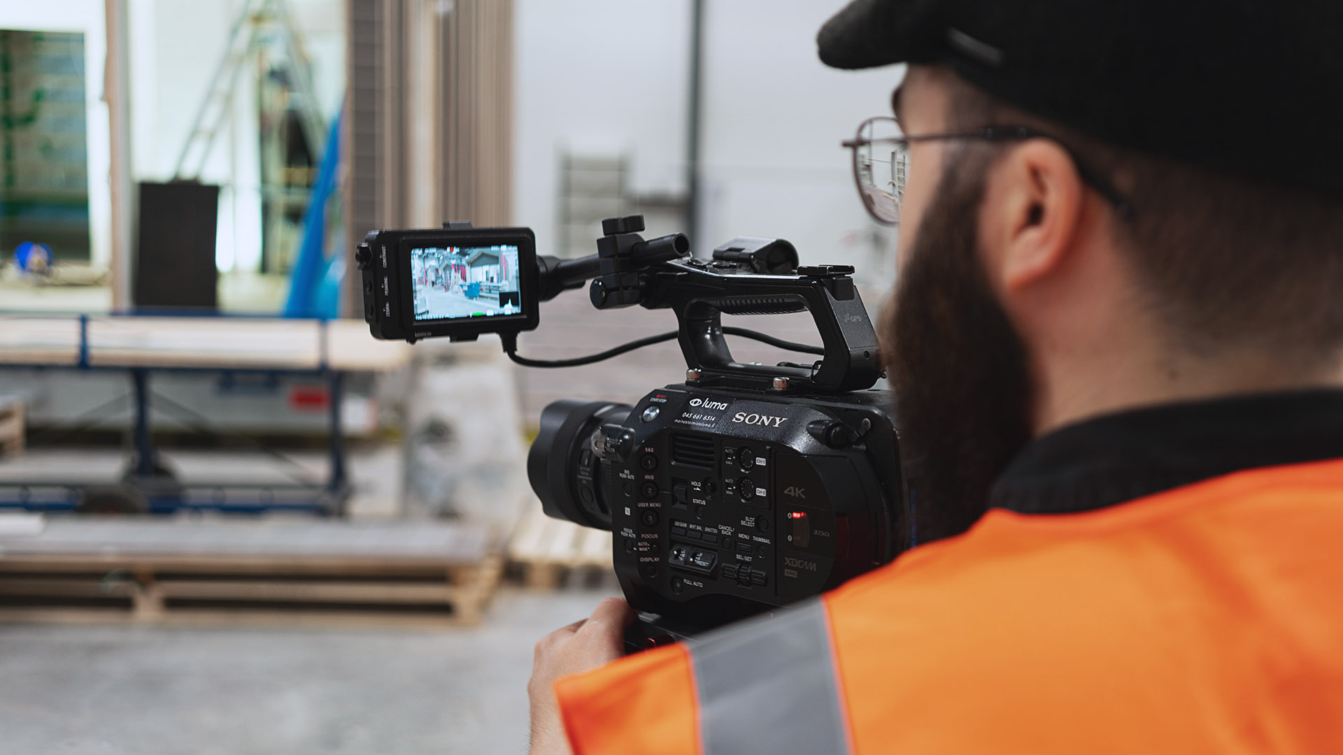Luma Creativen blogiartikkelin pääkuva, joka on otettu videokuvaajan olkapään yli teollisuusympäristössä. Kuva visualisoi käytännön videotuotantotyötä ja yritysvideoiden kuvauksiin valmistautumista.
